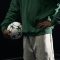A person in sports attire holds a soccer ball in a dynamic pose on a dark background.